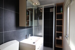 Une salle de bain moderne avec un lavabo blanc, une douche à parois de verre et une étagère intégrée en bois.