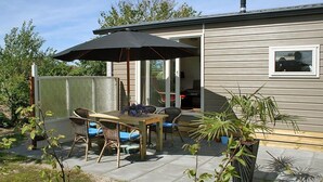 Une terrasse avec une table et des chaises, un grand parasol et des plantes en pot.