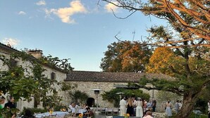 An outdoor dining area with tables set up for a meal, surrounded by stone buildings and trees. - Holiday home in Pardaillan with private pool (Pardaillan)