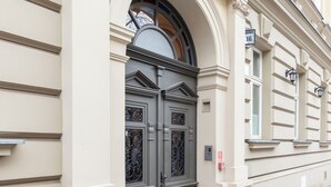 Een gevel met een grote, versierde hoofdingang, een klein raam met een metalen traliewerk en een straatnaambordje met het adres.