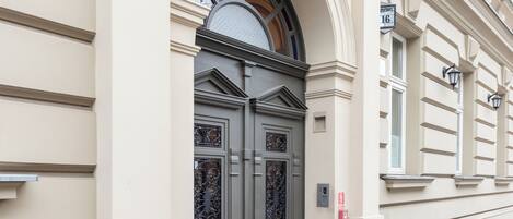 Une façade d’immeuble avec une grande porte d’entrée ornée, une petite fenêtre avec une grille métallique et un panneau de rue indiquant l’adresse.
