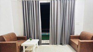 Una habitación con dos sofás marrones, una mesa de centro blanca y vistas a una piscina a través de cortinas grises.