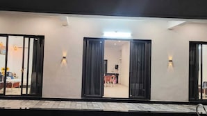 Exterior de un hotel con grandes puertas correderas de vidrio, zona de entrada con baldosas y lámparas fijadas a la pared.