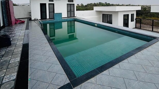 Una piscina en la azotea con una superficie de agua azul cristalina, rodeada por una solana con baldosas y un edificio blanco con ventanas de marco negro.