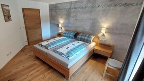 Un dormitori amb un llit de fusta, dues taules de nit, una petita taula i una làmpada penjada a la paret, i una porta.