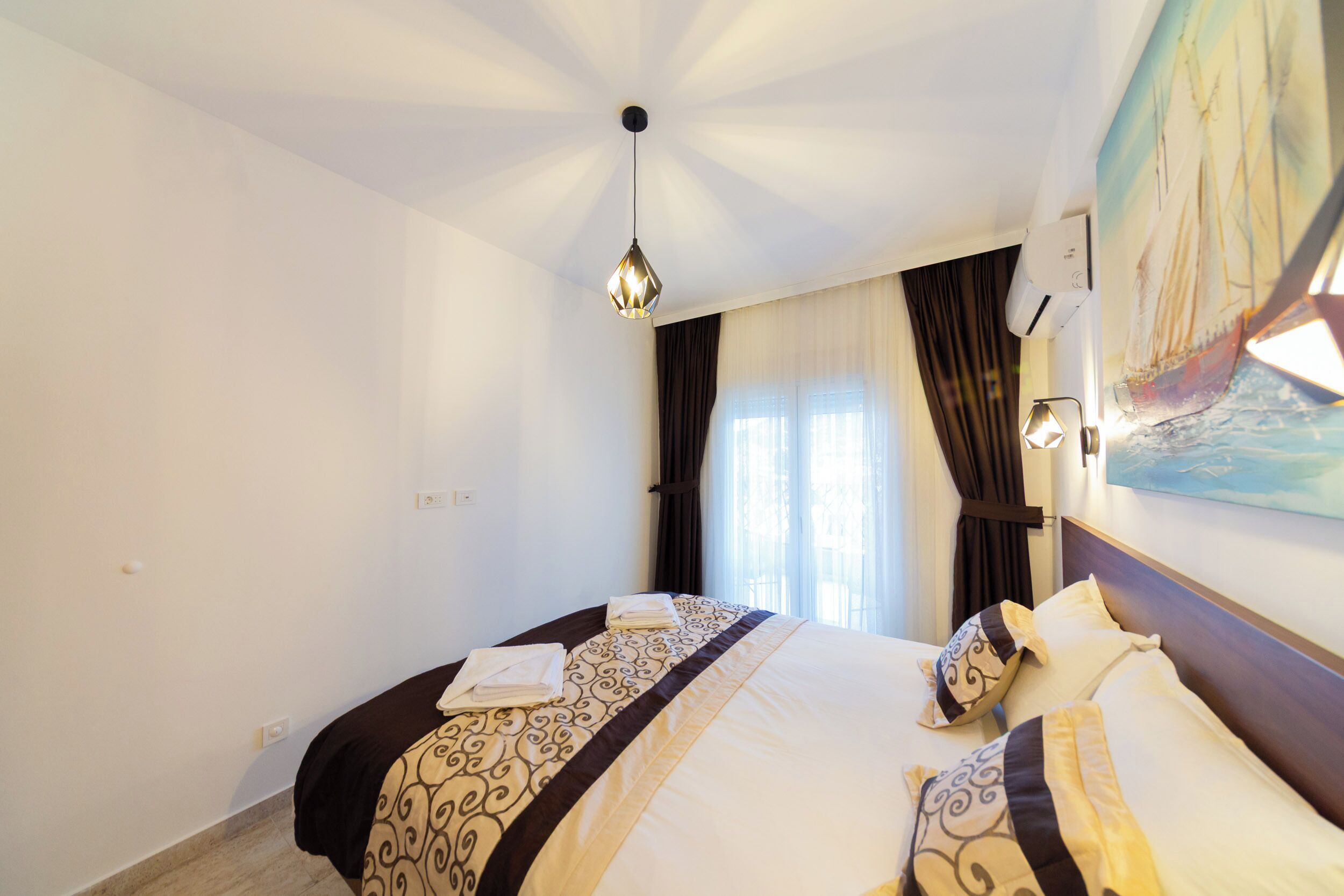 Een hotelkamer met een groot bed, een plafondlamp, een schilderij aan de muur en een raam met gordijnen.