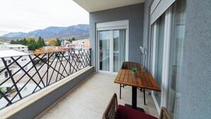 A balcony with a wooden table and chairs, a potted plant, and a view of the city and mountains in the background. - Lovely 2-bedroom apartment with AC in enchanting Sutomore (Sutomore)