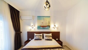 A neatly made bed with a patterned bedspread, two bedside tables with lamps, a wall-mounted air conditioner, and a painting of a sailboat. - Lovely 2-bedroom apartment with AC in enchanting Sutomore (Sutomore)