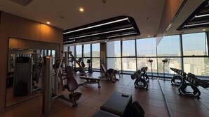 Une salle de sport équipée de divers appareils d’exercice, dotée de grandes fenêtres et d’un plafond haut.