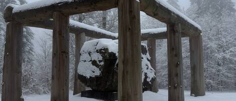 A wooden gazebo in a snowy landscape with trees in the background.