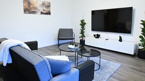 Una sala de estar moderna con un sofá, una mesita de centro, un televisor y dos plantas en macetas.