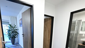 Un pasillo con suelo de madera, una planta en maceta, una cesta de mimbre y un banco de metal negro.