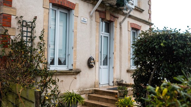 Un bâtiment sur lequel on peut lire l’inscription « Villa Eperonne », un escalier menant à une porte, et des plantes en pot au premier plan.