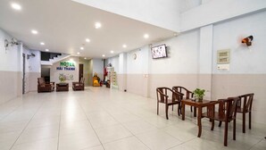Un vestíbulo de hotel con mostrador de recepción, sillas de madera, una mesa de comedor y una escalera que sube al piso superior.