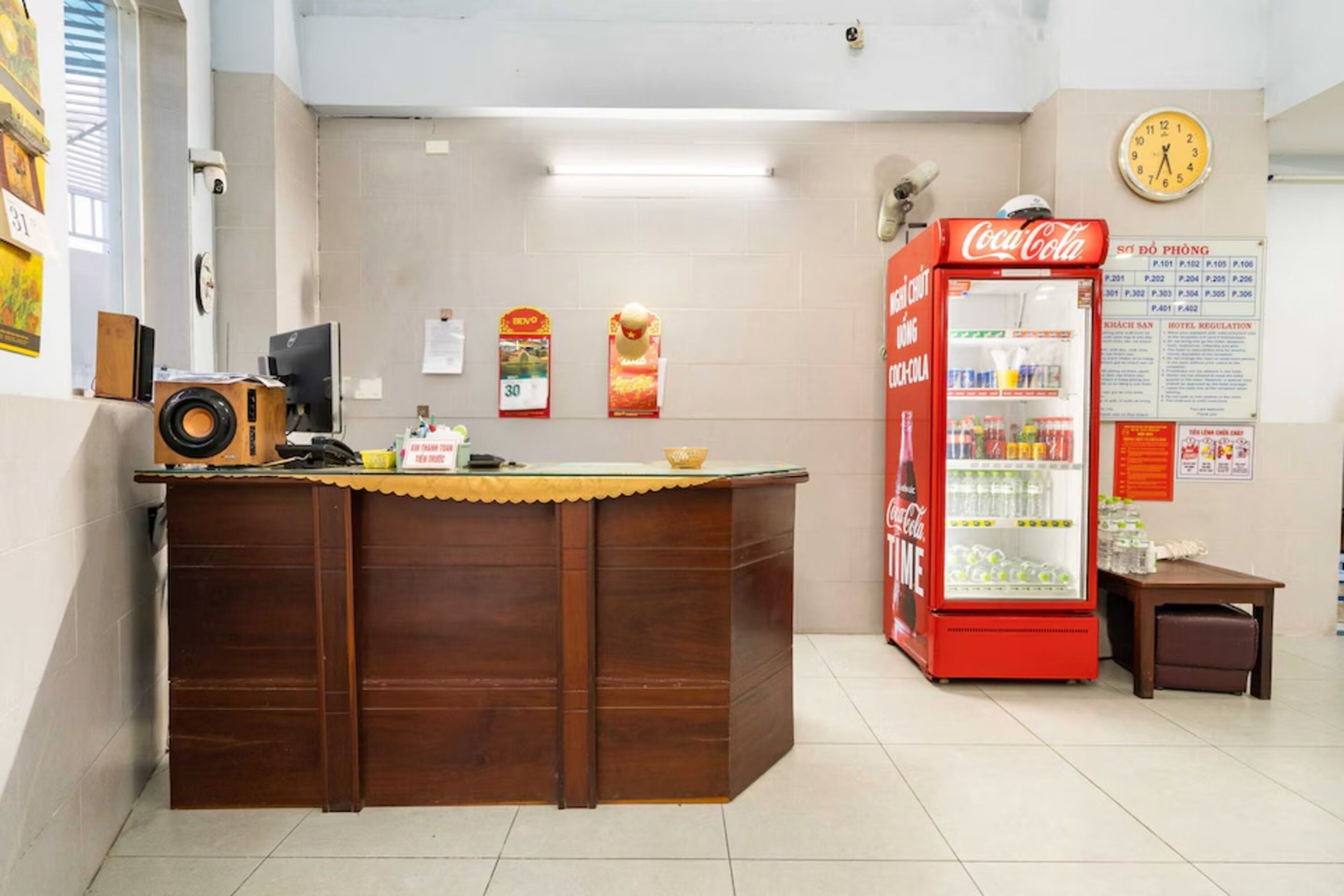 A reception desk with a Coca-Cola refrigerator, a clock, and a sign with hotel regulations.