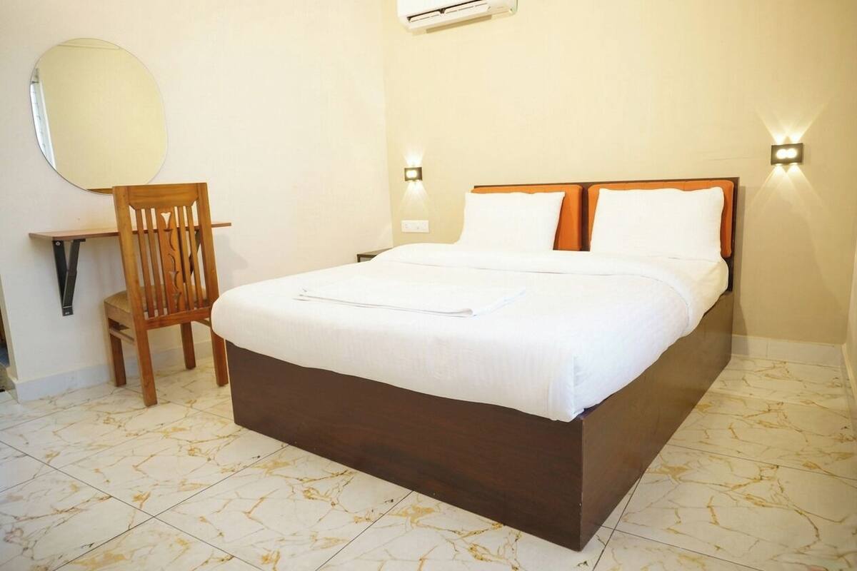 A hotel room with a bed, a chair, a mirror, and wall-mounted lights.