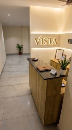 A reception desk with a wooden finish, a potted plant, and a sign that reads 'VISTA.'. Vista by Booksy One
