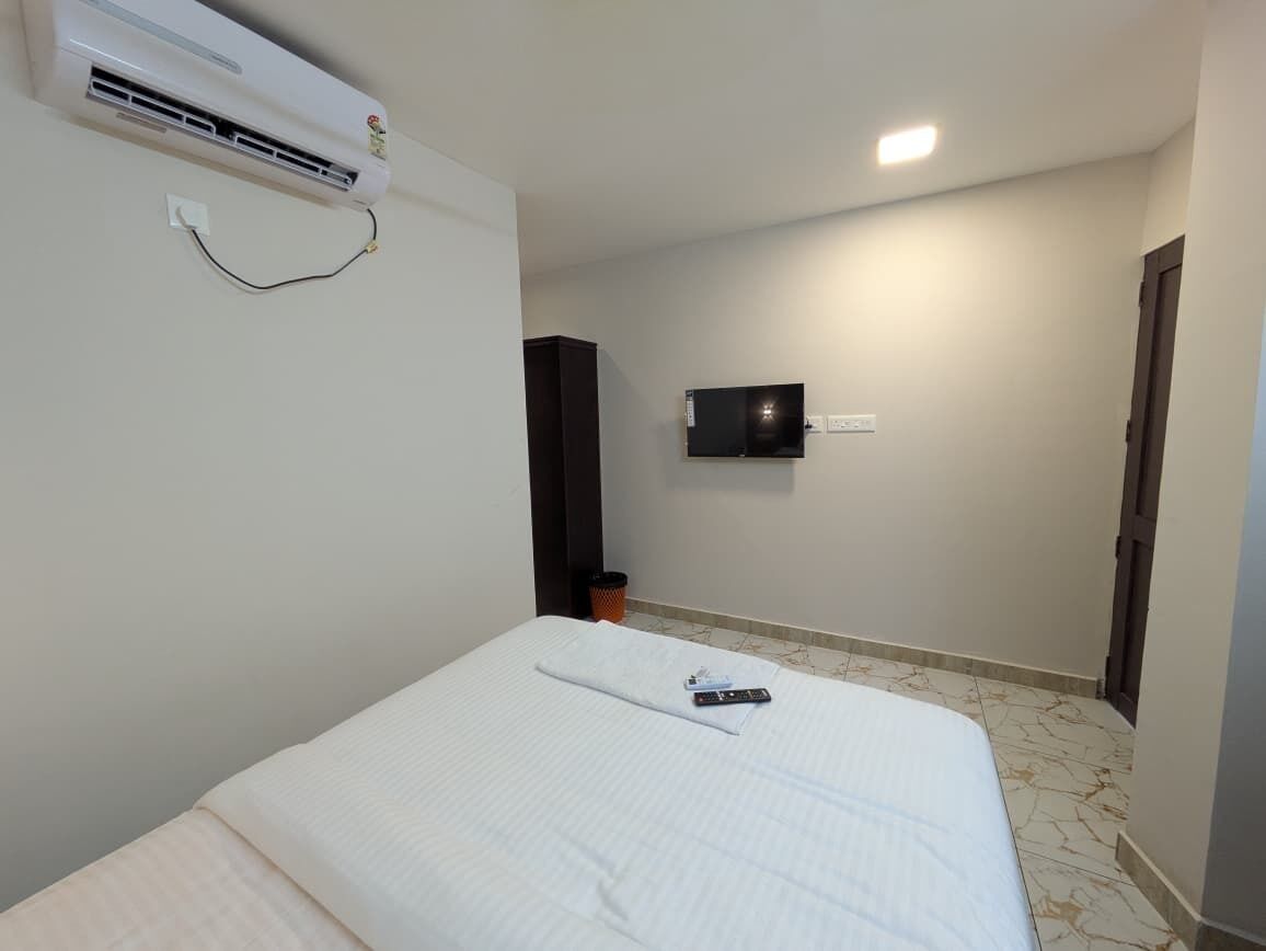 Una habitación de hotel con cama, aire acondicionado, televisión en la pared y una puerta.