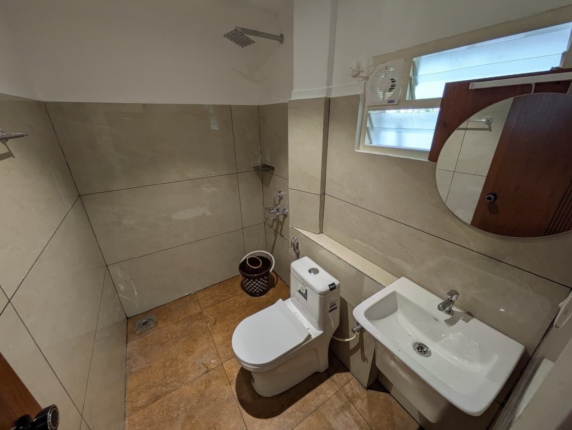 A bathroom with a toilet, sink, shower, and a window providing natural light.