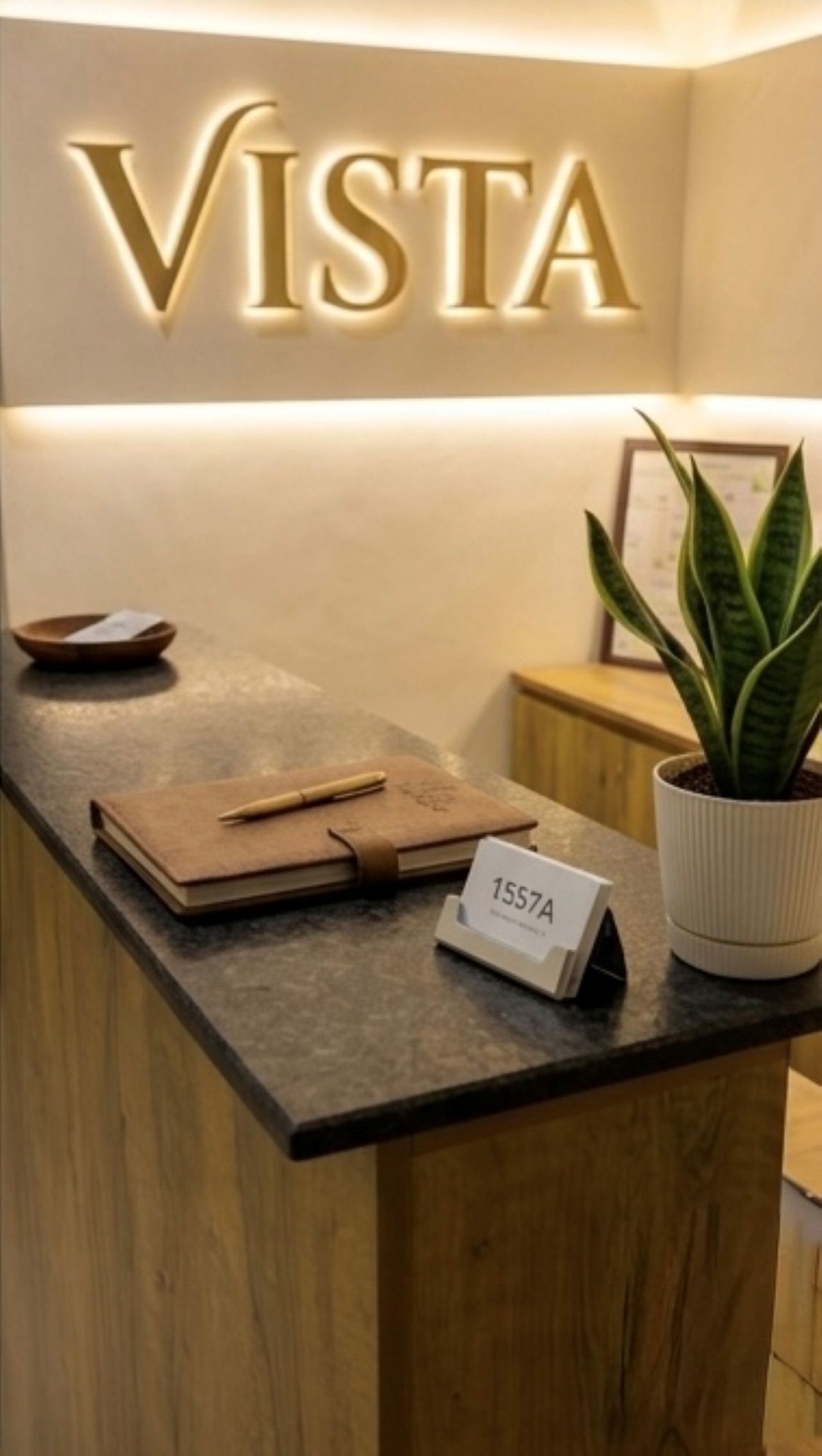 Mostrador de recepción con un cartel que dice 'VISTA', una planta, una libreta, un bolígrafo y una tarjeta de identificación.. Vista by Booksy One