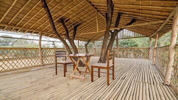 Una terraza de bambú con una mesa y sillas, rodeada por una valla de madera y árboles.