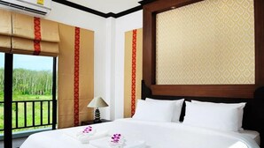 A hotel room with a large bed, a nightstand with a lamp, and a view of a lush garden through a sliding door. - Baan Narakorn (Krabi)