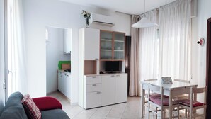 Uma sala de estar moderna com sofá, mesa de jantar com cadeiras, cozinha compacta e televisão.