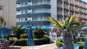 Um hotel com vários andares, varandas, área de piscina com guarda-sóis e palmeiras.