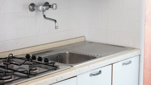 Una cocina con armarios blancos, un lavamanos de acero inoxidable y una estufa a gas.