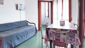 Une pièce avec un canapé bleu, une table recouverte d’une nappe à motifs floraux et un luminaire au plafond.