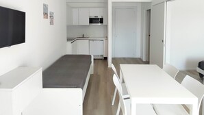Une chambre moderne et minimaliste, équipée d’un lit, d’une table à manger et d’un coin cuisine.