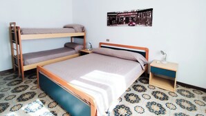 Een kamer in slaapzaalstijl met stapelbedden, een enkele bed, een nachtkastje, een lamp en een aan de muur bevestigd schilderij.