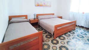 A room with two wooden beds, a nightstand with a lamp, a wall-mounted picture, and patterned floor tiles. - Comfortable apartment near the beach (Lido di Jesolo)