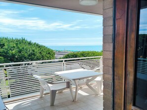 A balcony with a table and chairs, overlooking a beach and greenery. - Cozy studio with balcony (Lido di Jesolo)