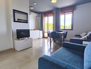 A modern living room with a flat-screen TV, a sofa, a dining table with chairs, and a kitchen area with cabinets and a refrigerator. - Cozy studio with balcony (Lido di Jesolo)