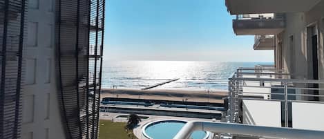 A view from a balcony overlooking a beach with a pool and a clear sky.