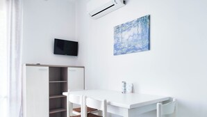 A white room with a desk, chairs, a wardrobe, a flat-screen TV, and a painting on the wall. - Comfortable studio by the sea (Lido di Jesolo)