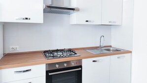 A modern kitchen with white cabinets, a stainless steel stove, a sink, and a wooden countertop. - Comfortable studio by the sea (Lido di Jesolo)