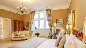 A spacious bedroom with a large bed, a sitting area with a sofa and armchair, a chandelier, and a window with curtains. - Rudha Na Craig (Inveraray)
