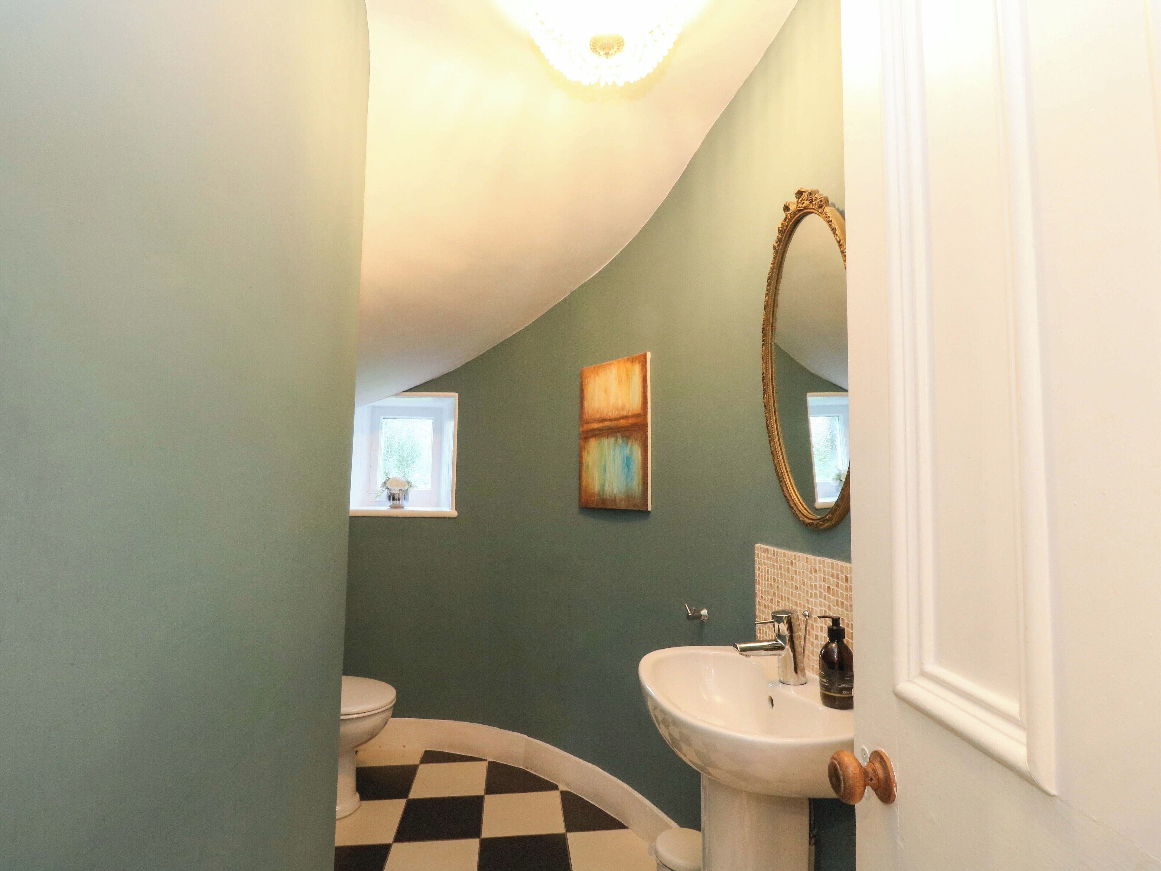 A bathroom with a white sink, a white toilet, a small window with a plant, and a painting on the wall.