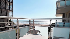 A balcony with a table and chairs, overlooking a beach with a clear sky. - Cozy flat with balcony by the sea (Lido di Jesolo)