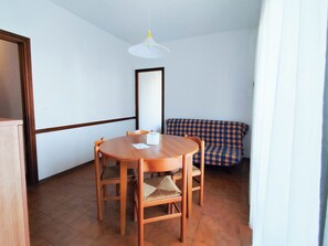 A small, cozy room with a round wooden table and four chairs, a checkered sofa, and a white pendant light. - Spacious apartment with balcony by the sea (Lido di Jesolo)