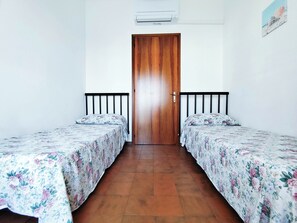 A room with two single beds, a wooden door, a white wall, and a small air conditioning unit. - Spacious apartment with balcony by the sea (Lido di Jesolo)