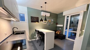 Et kompakt køkken med en central ø, et spiseområde med stole, og en opholdsstue med en sofa.