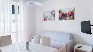 A room with a dining table, a sofa, a TV, and two wall-mounted pictures. - Comfy apartment with pool access (Lido di Jesolo)