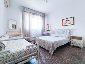 Una habitación de hospital con dos camas, una mesita de noche, un espejo y una ventana con cortinas.