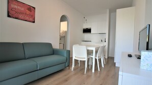 En moderne stue med en turkis sofa, et spiseområde med hvide stole og et køkken med hvide skabe.