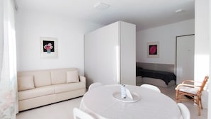 Een moderne, minimalistische kamer met een ronde eettafel, een bank, een bed en een kledingkast.