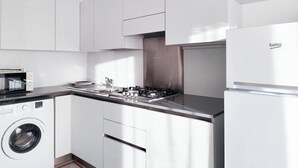 Een moderne keuken met witte kastjes, een ingebouwde wasmachine, een magnetron, een gasfornuis en een koelkast.