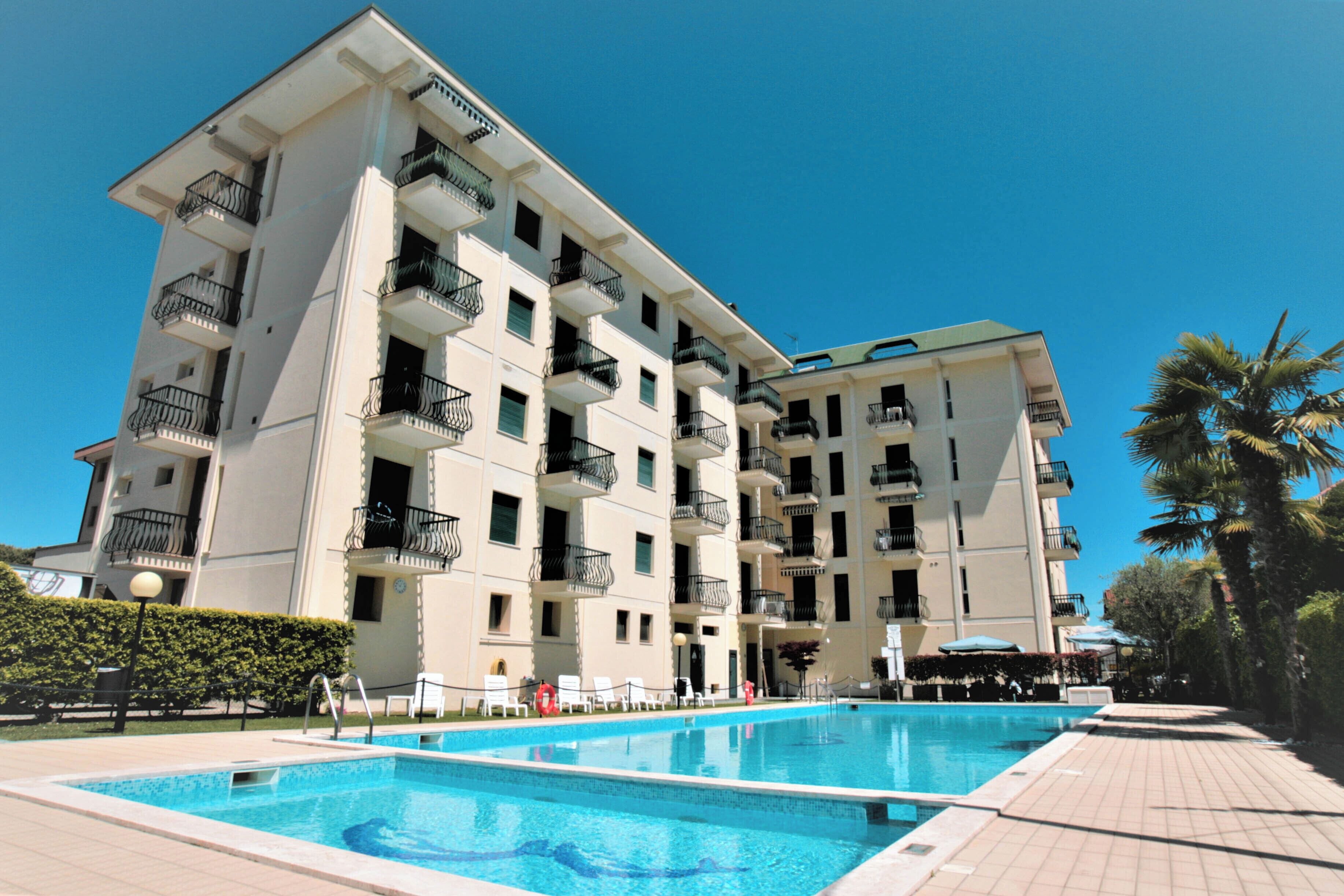 Ein mehrstöckiges Hotel mit Schwimmbad, Balkonen und blauem Himmel.